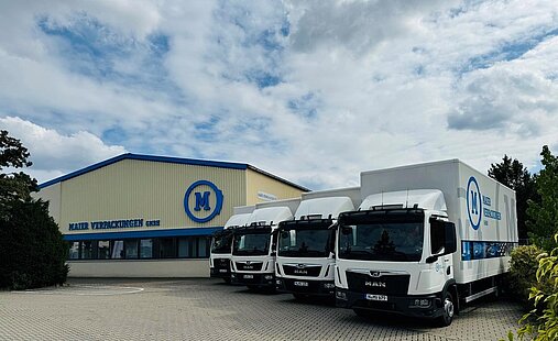 Vier Lastwagen stehen vor einer Lagerhalle 